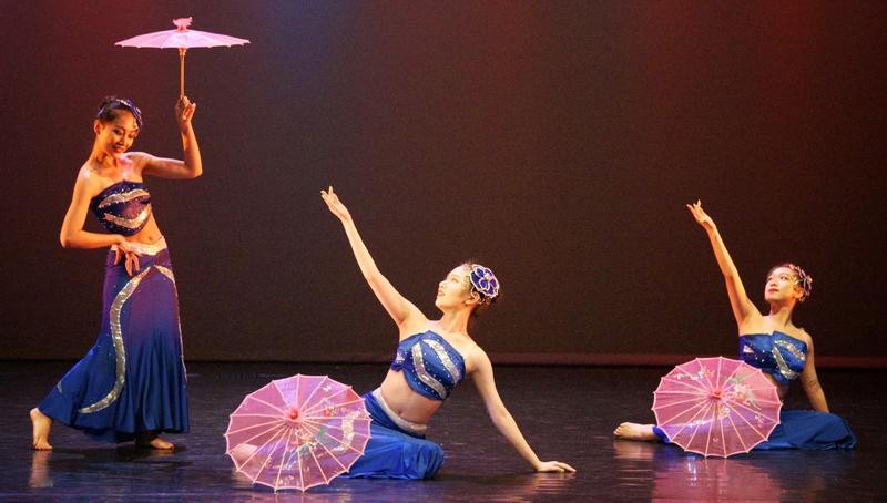 Three dancers in blue Dai costumes with pink parasols