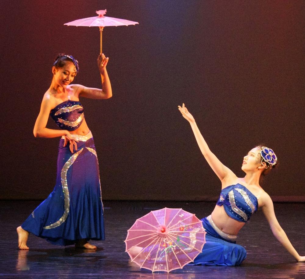 Dancers in blue Dai costumes performing with pink parasols