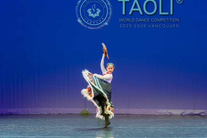 A YiYe student mid-turn in a Tibetan costume with a striped, fur-trimmed skirt at the TAOLI World Dance Competition in Vancouver
