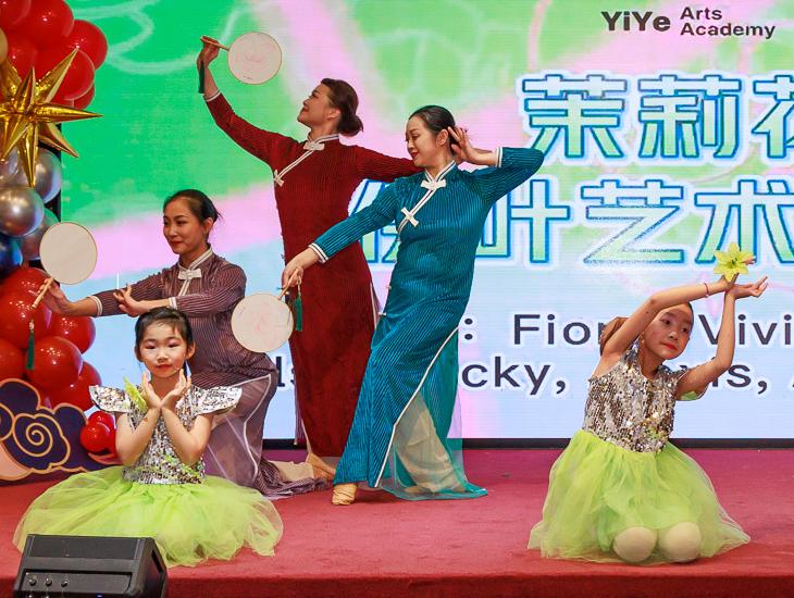 YiYe teachers in qipao dancing with round fans while young students pose in front